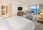 A hotel room with a large bed, a television, a desk with a lamp, a chair, and a view of the ocean.