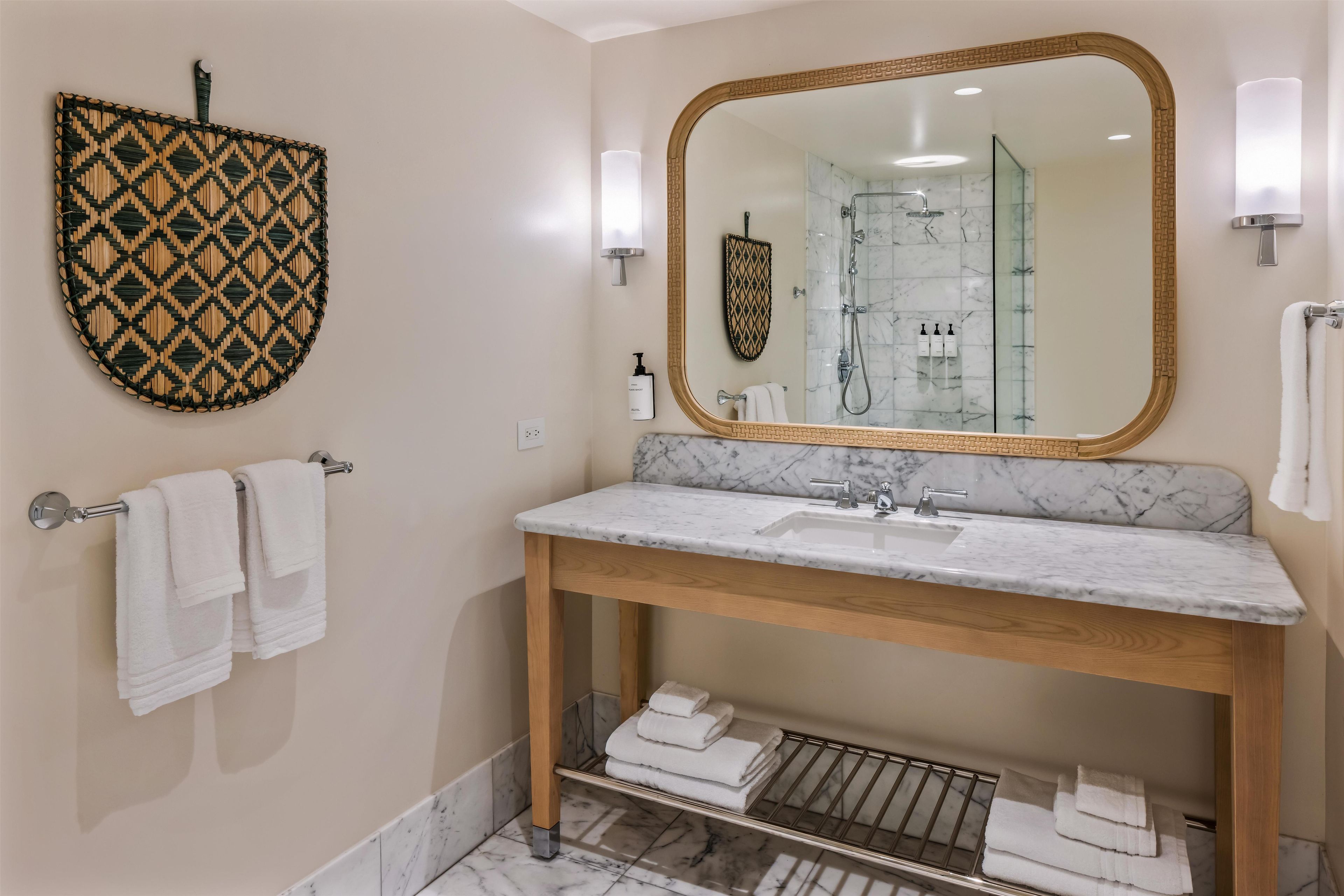 A bathroom with a large mirror, two sinks, a towel rack, and a shower area.