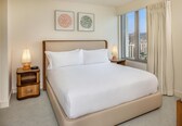 A hotel room with a large bed, two bedside lamps, a nightstand, and a window with a city view.
