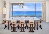 A dining area with a large table and chairs, a chandelier, and a view of the ocean.
