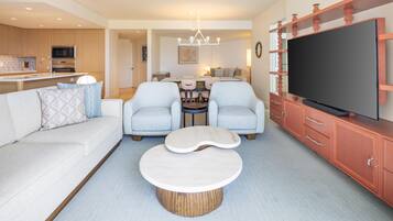 A modern living room with a sofa, two armchairs, a coffee table, a TV, and a kitchen area in the background.