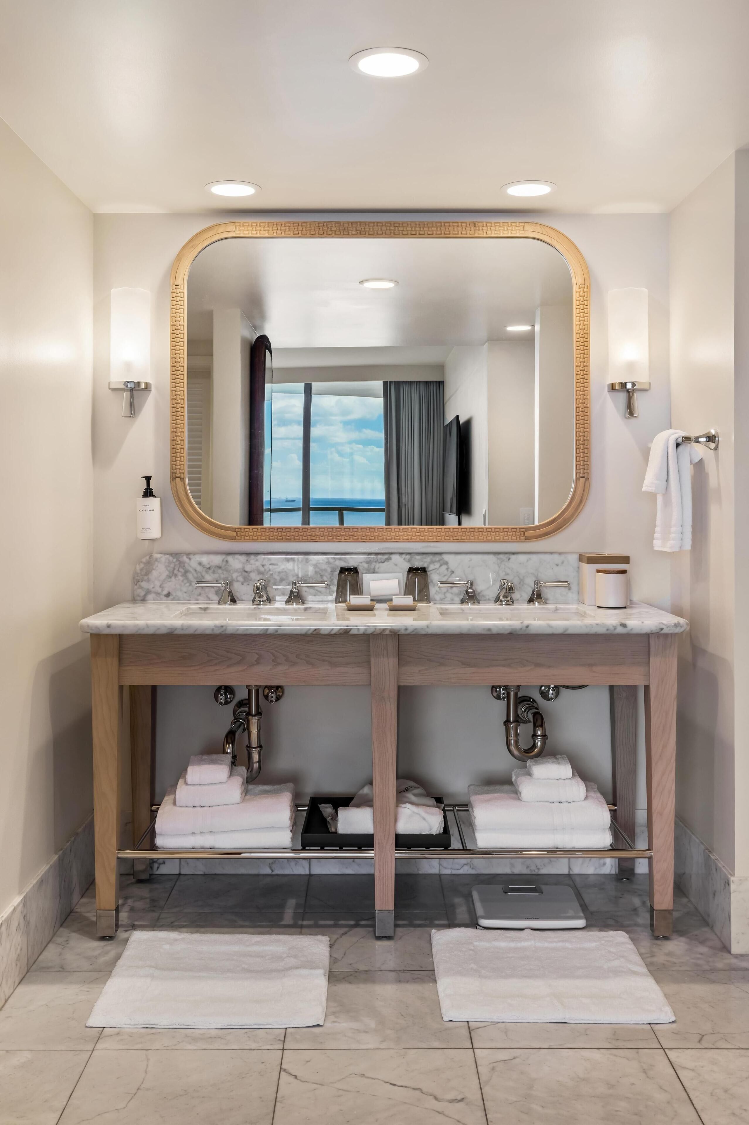 Un baño moderno con un espejo grande, lavamanos dobles y vista al mar desde la ventana.