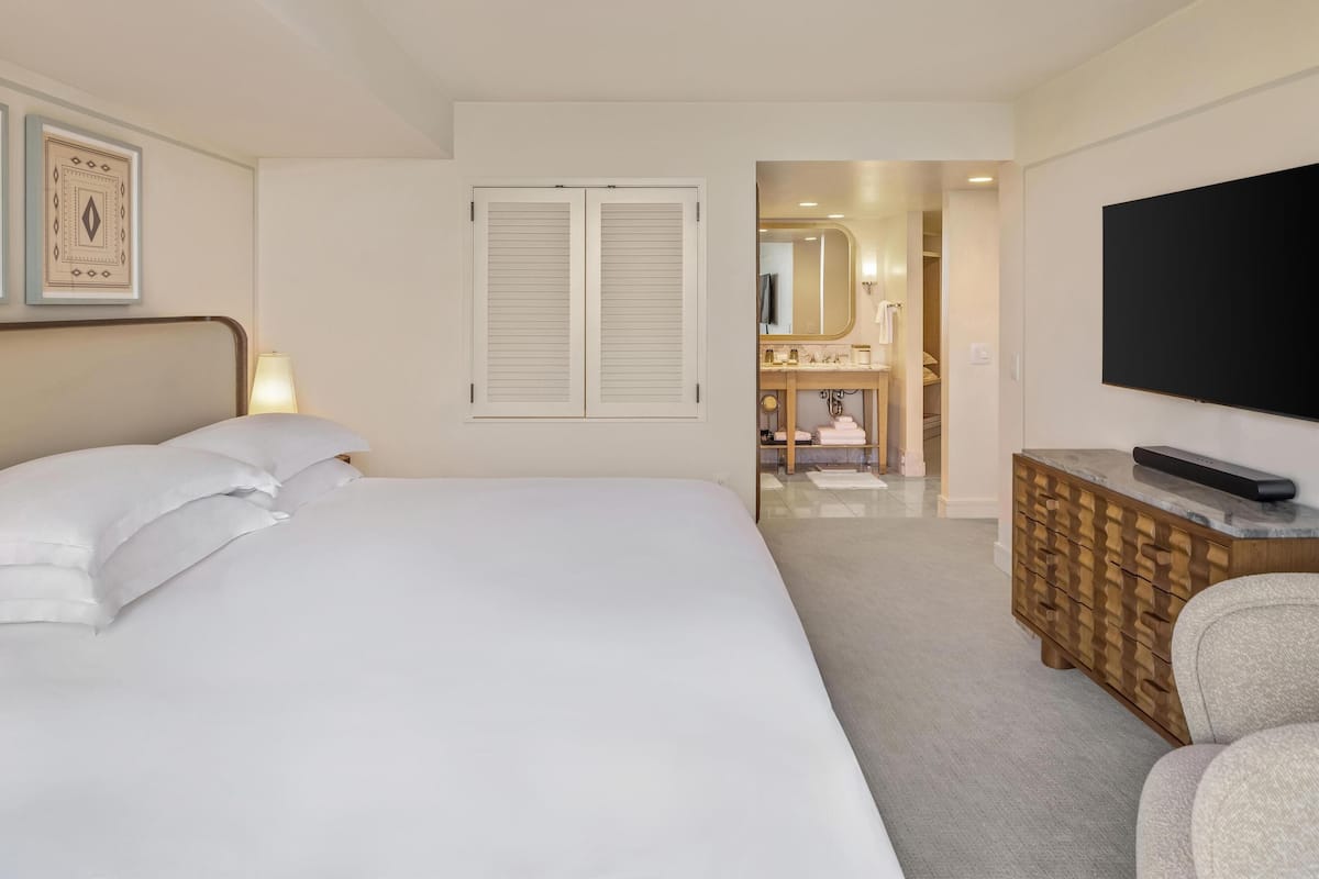 Een hotelkamer met een bed, een televisie, een houten dressoir en een badkamer zichtbaar door een geopende deur.