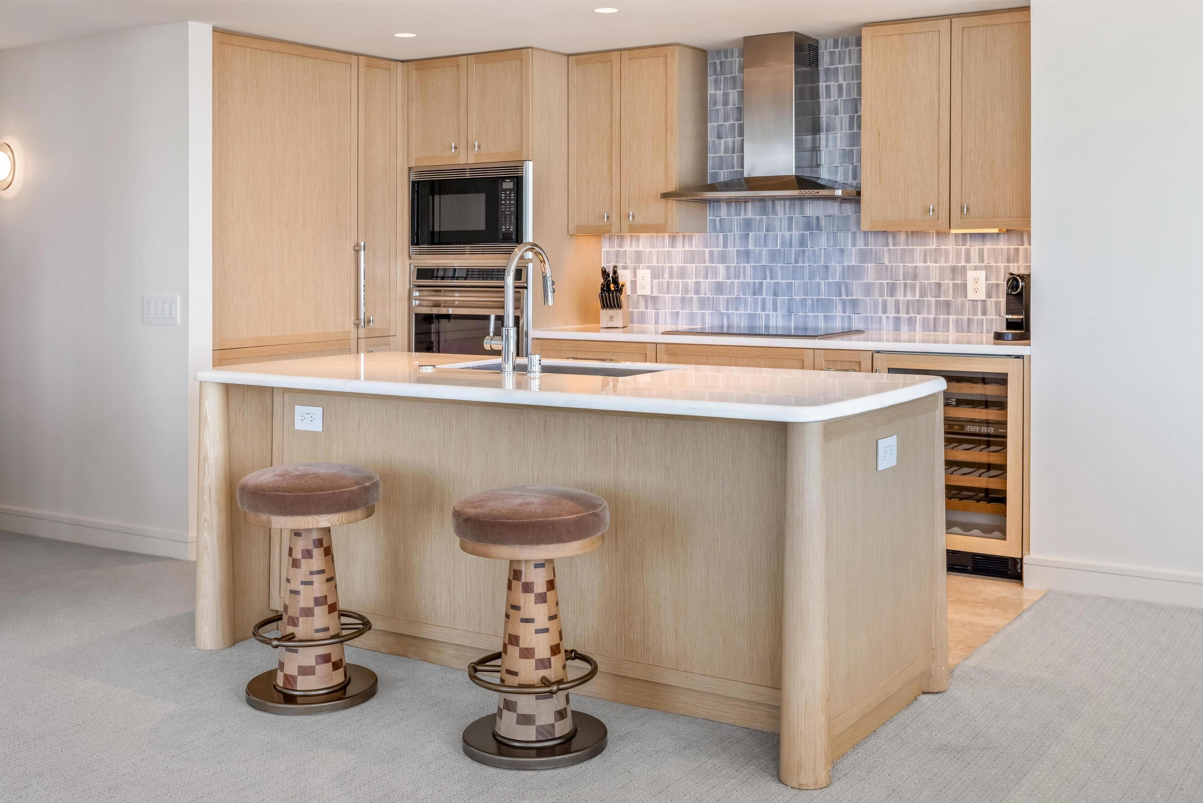 A kitchen with wooden cabinets, a built-in microwave, a stainless steel range hood, and a large island with stools.