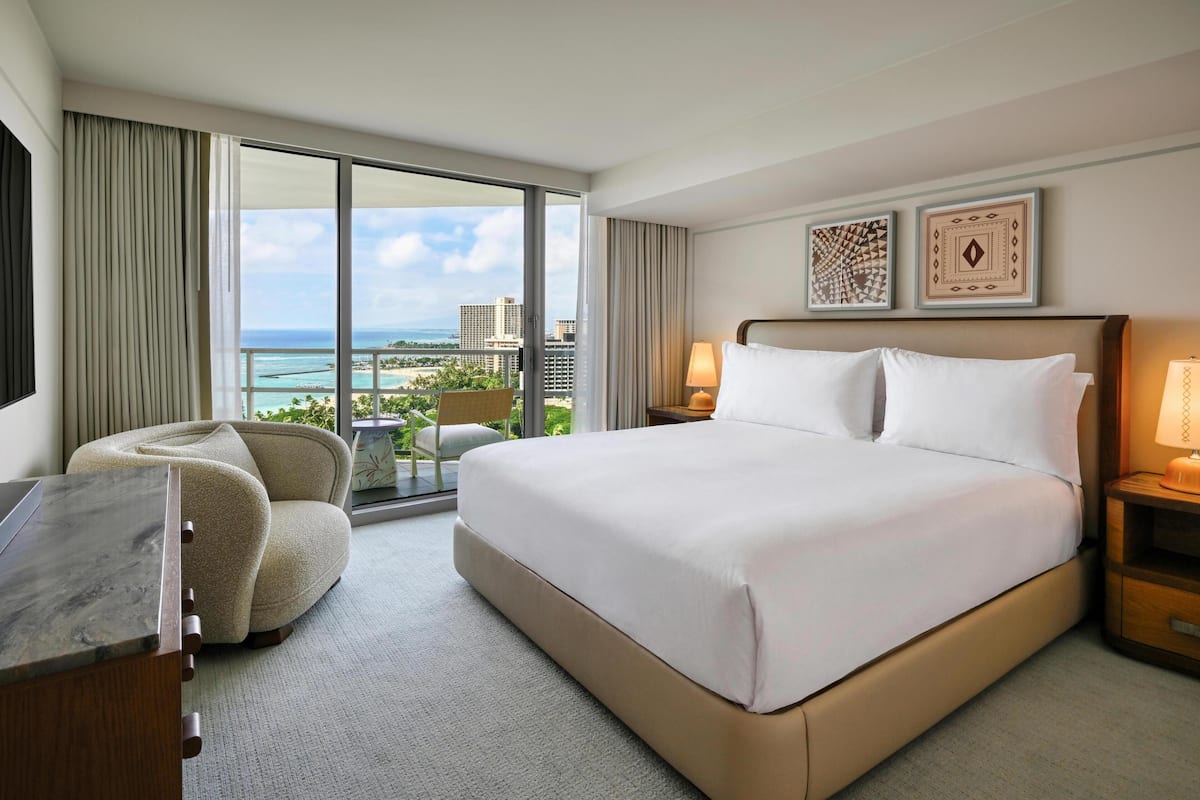 Een hotelkamer met een groot bed, een bureau, een stoel en uitzicht op de oceaan.