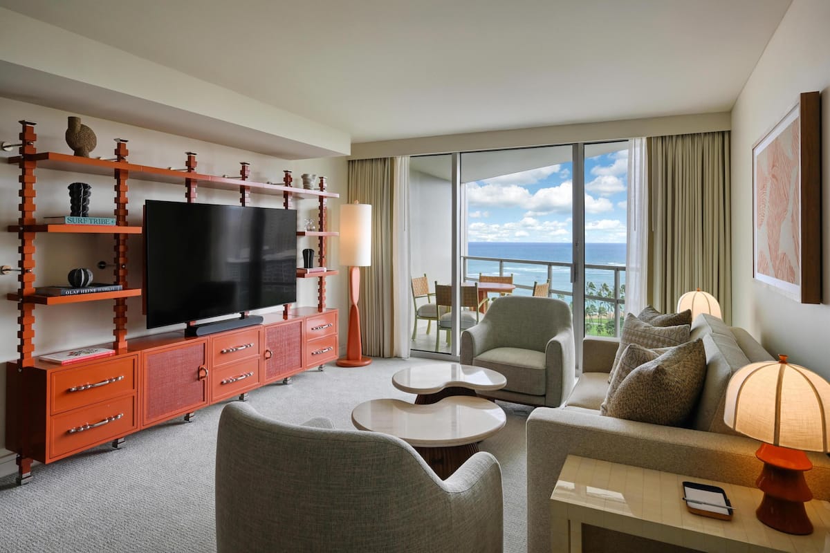 Een hotelkamer met een televisie, bank, fauteuil en een balkon met uitzicht.