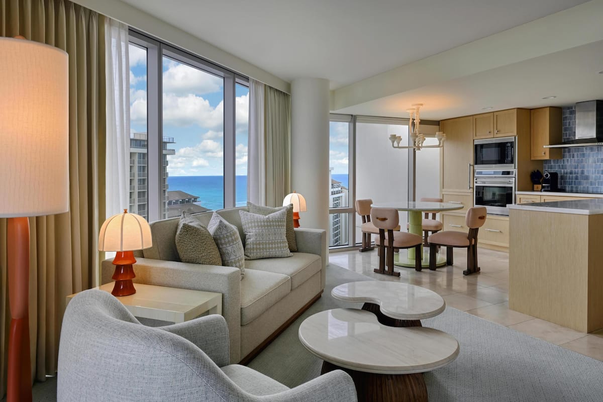 Een moderne hotelkamer met balkon, een bank, een eettafel en een kitchenette.