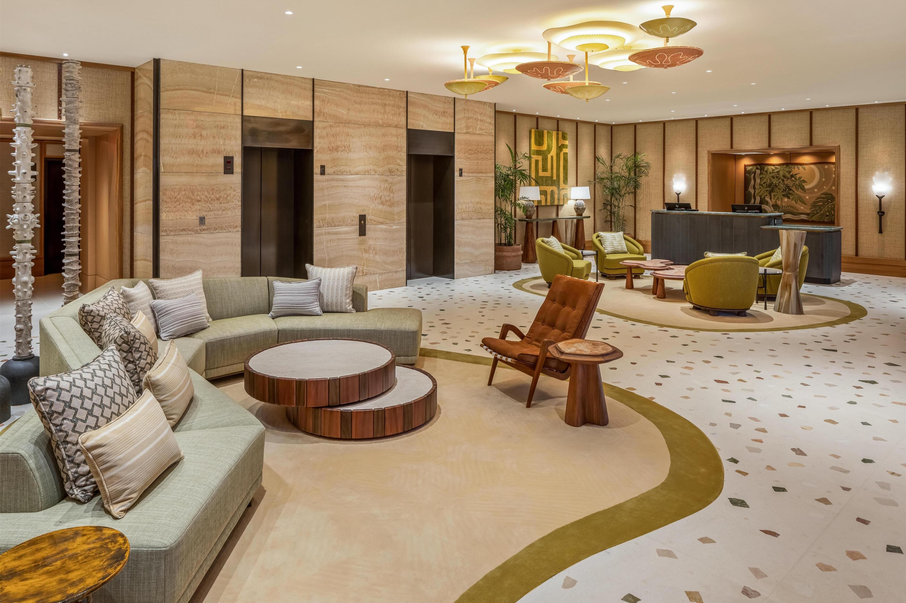A modern lobby with a sectional sofa, a round wooden coffee table, a green armchair, and a reception desk.