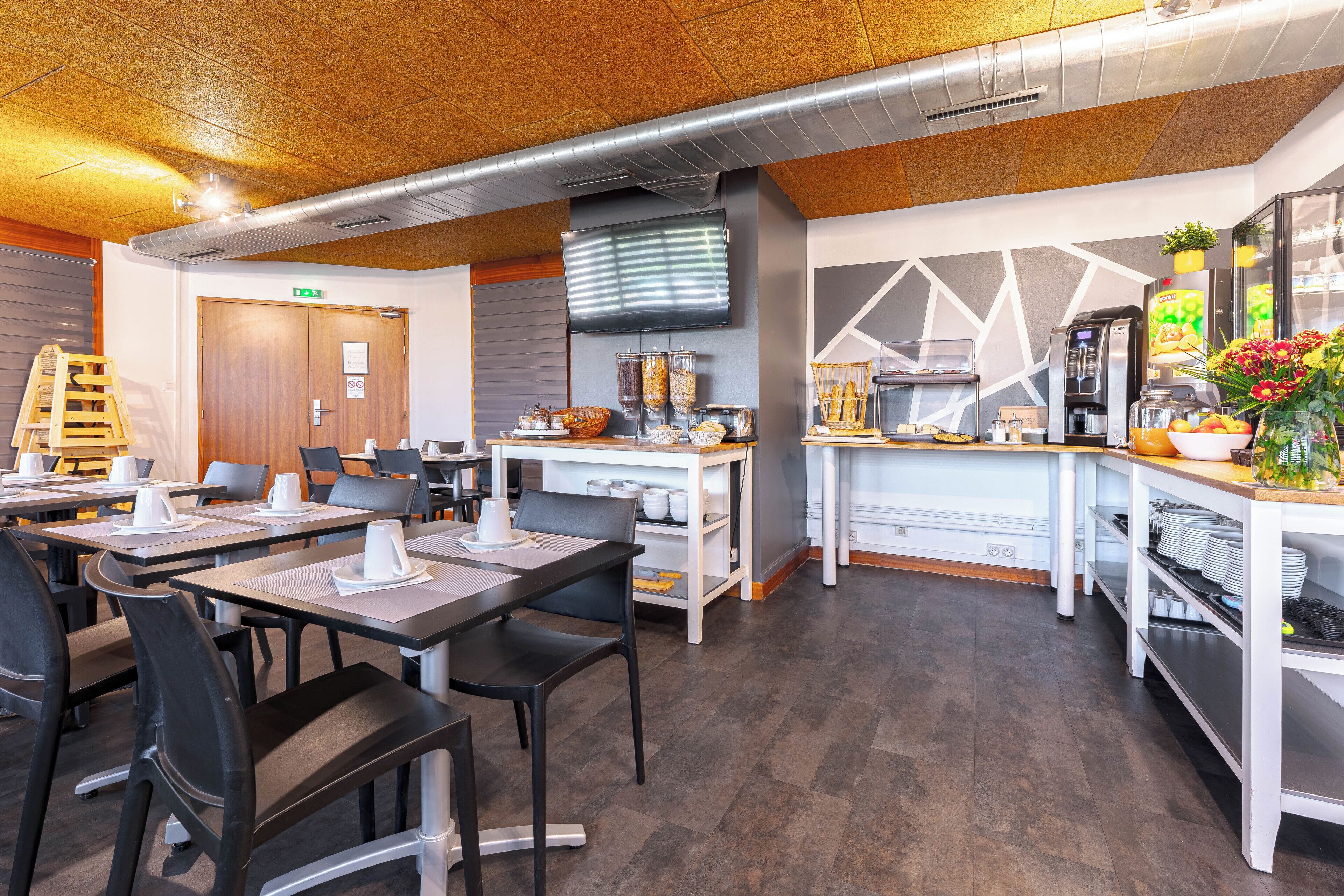 A modern restaurant with a wooden ceiling, a flat-screen TV, and a buffet area with various food items.