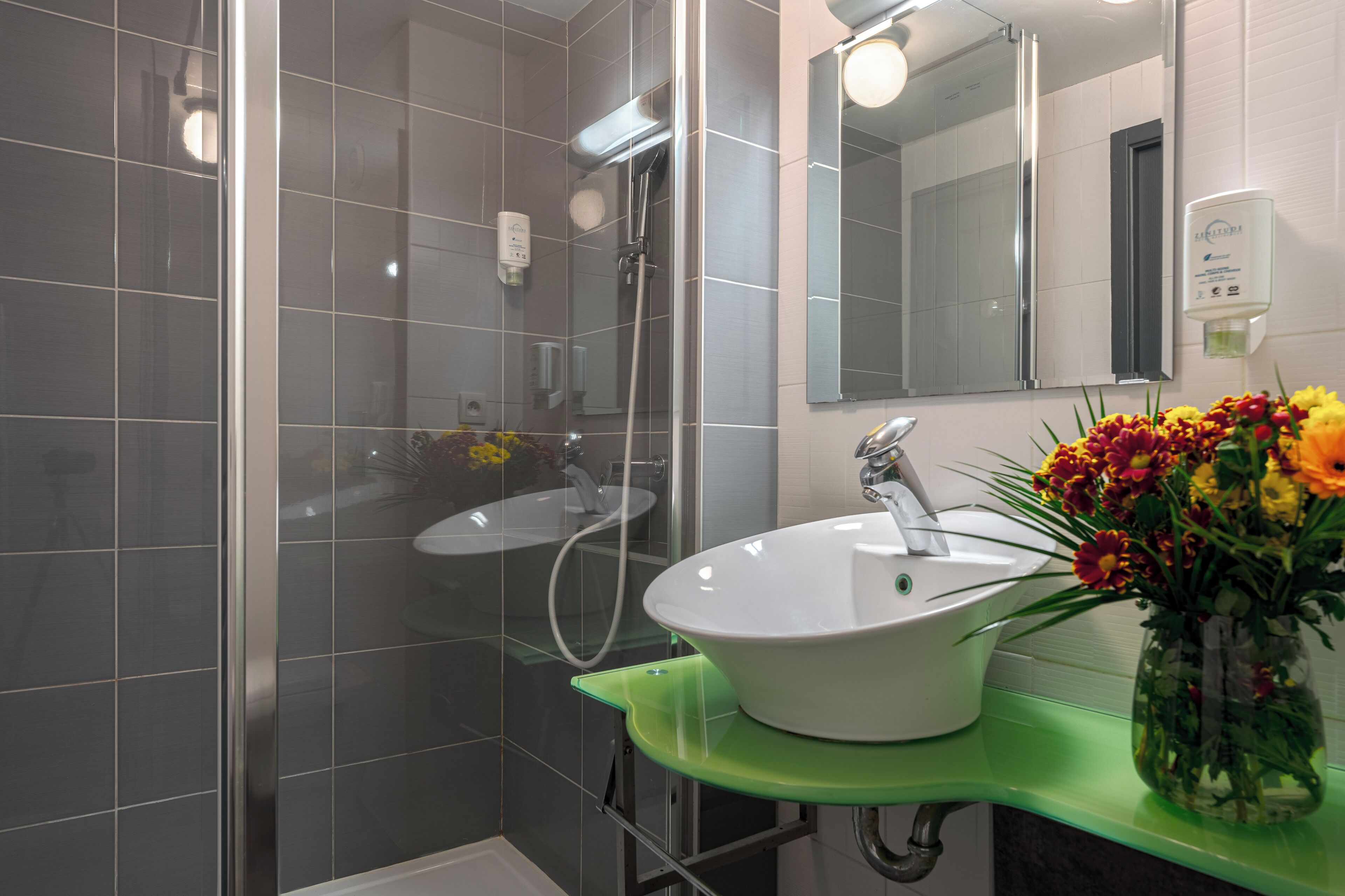 Ein modernes Badezimmer mit einer Duschkabine aus Glas, einem weißen Waschbecken mit grüner Arbeitsplatte und einem Spiegel über dem Waschbecken.