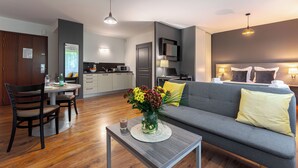 Een moderne woonkamer met een grijze bank, een eettafel met stoelen, een bijzettafel met een bloevas en een keuken op de achtergrond.