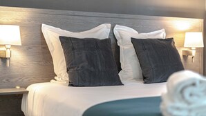Een net opgemaakt bed met witte en donkergrijze kussens, twee bedlampen en een houten hoofdbord.