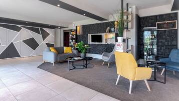 Una sala de estar moderna con un sofá gris, un sillón amarillo y una mesa de centro. Hay un televisor montado en la pared y una estantería con varios objetos.