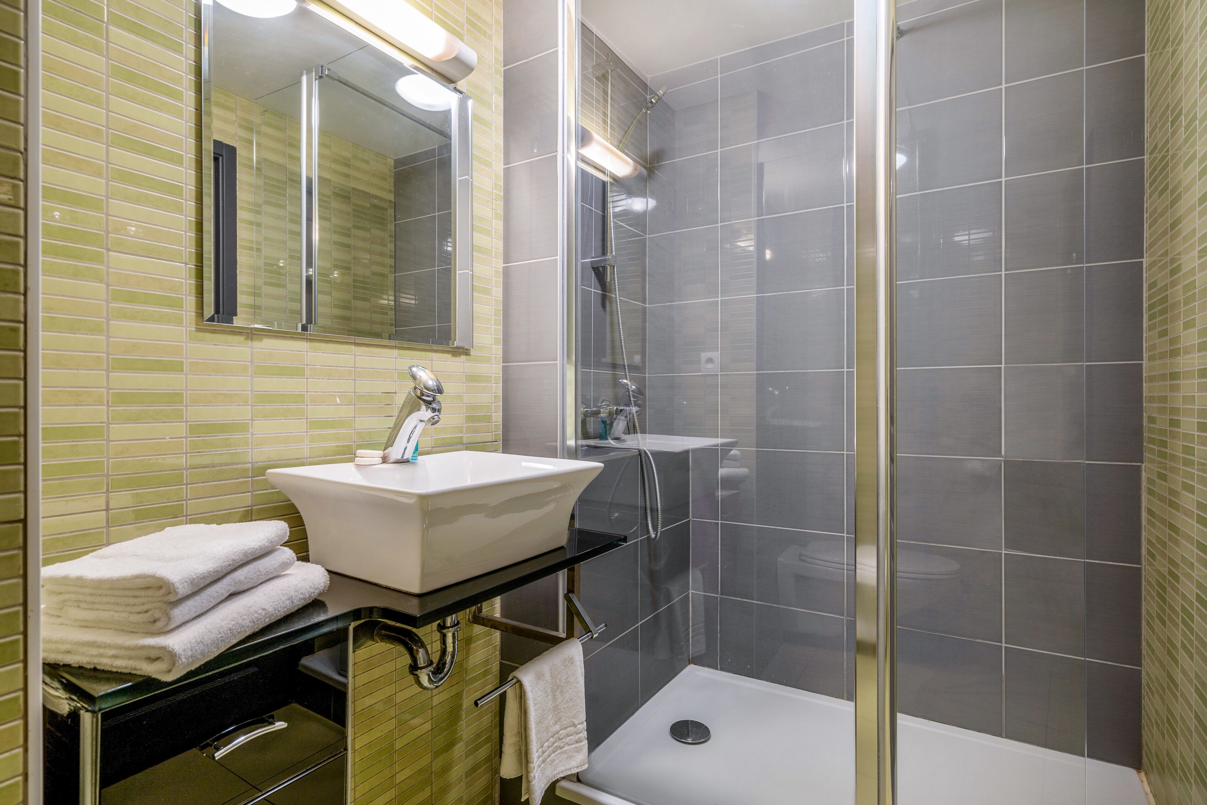 A modern bathroom with a glass-enclosed shower, a white sink, and a mirror above it.