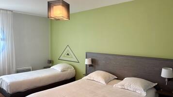 Habitación de hotel con dos camas individuales, una pared de acento verde, un adorno geométrico en la pared y una lámpara colgante.