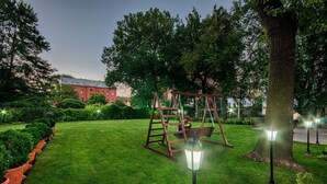 Un jardín bien cuidado con un columpio, setos ordenados y un gran árbol.