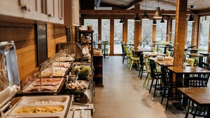 Zona de buffet con diversas opciones de comida, paredes de madera y ventanas amplias.