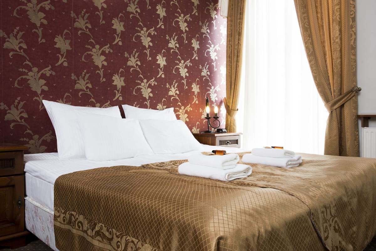 A neatly made bed with white linens, a brown patterned bedspread, and a bedside table with a lamp and folded towels.
