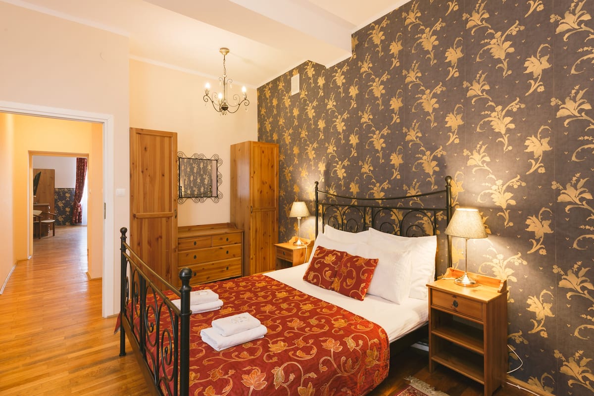 A bedroom with a wooden bed, two bedside tables with lamps, a wooden wardrobe, and a chandelier.