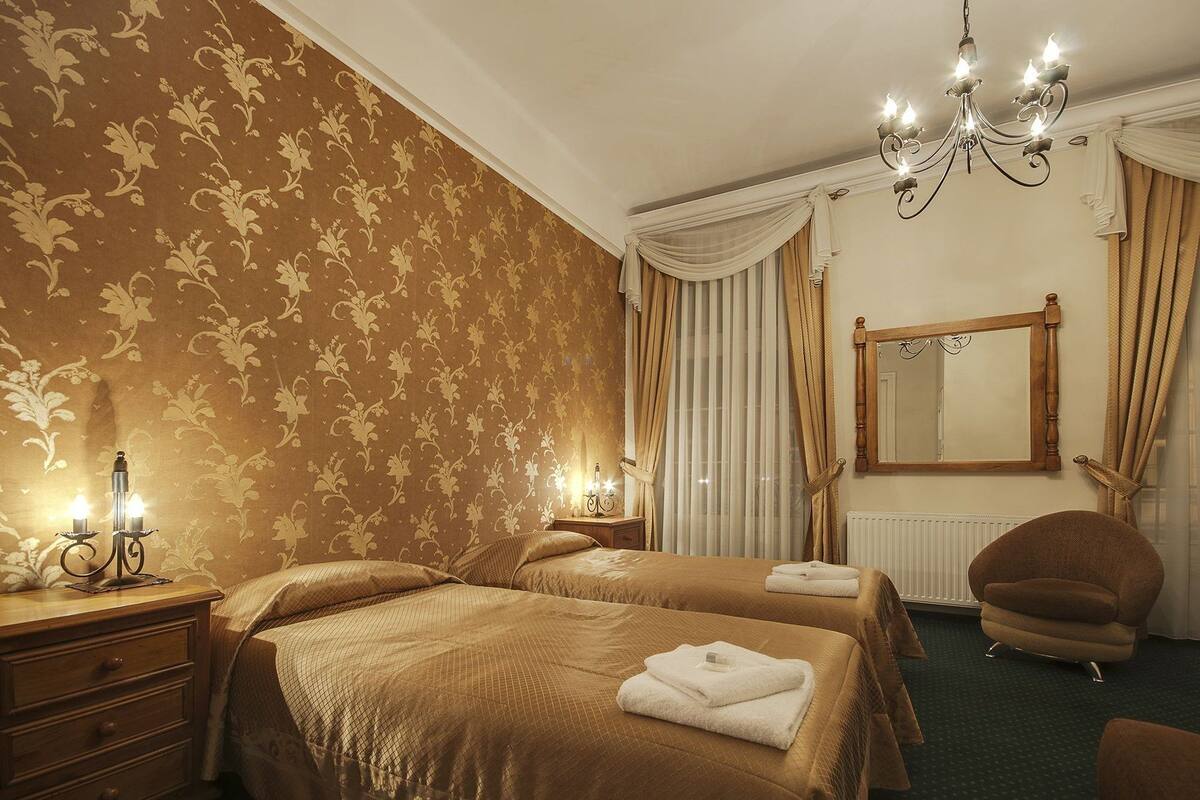 A hotel room with two beds, a chandelier, a mirror, and a chair.