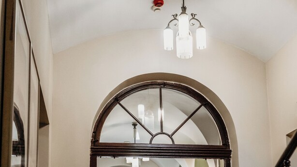 Un amplio pasillo con un arco de entrada a una habitación, una escalera con barandillas decoradas y un candelabro.