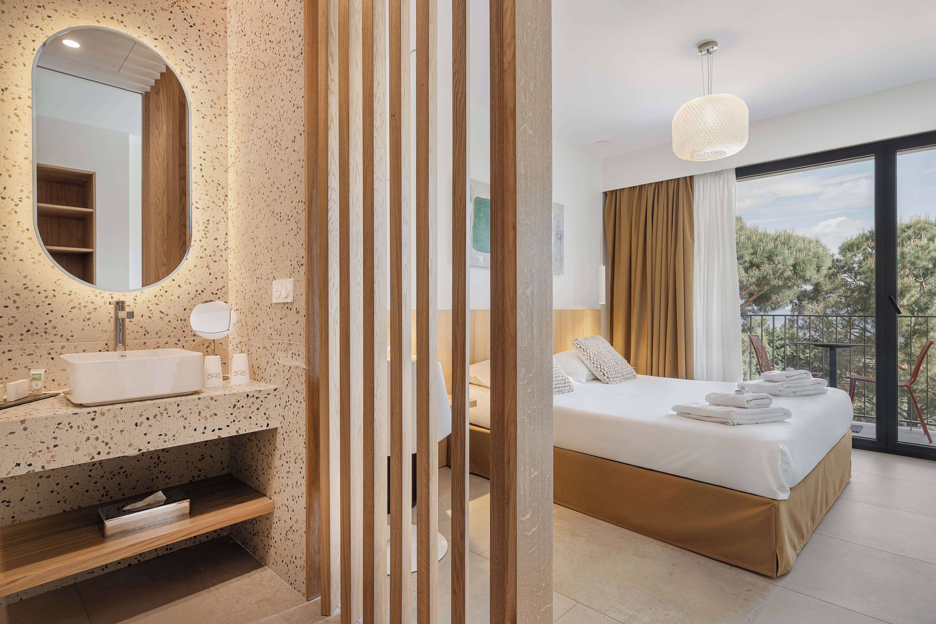 Quarto de hotel moderno com uma cama grande, banheiro com pia independente e varanda com vista para árvores.