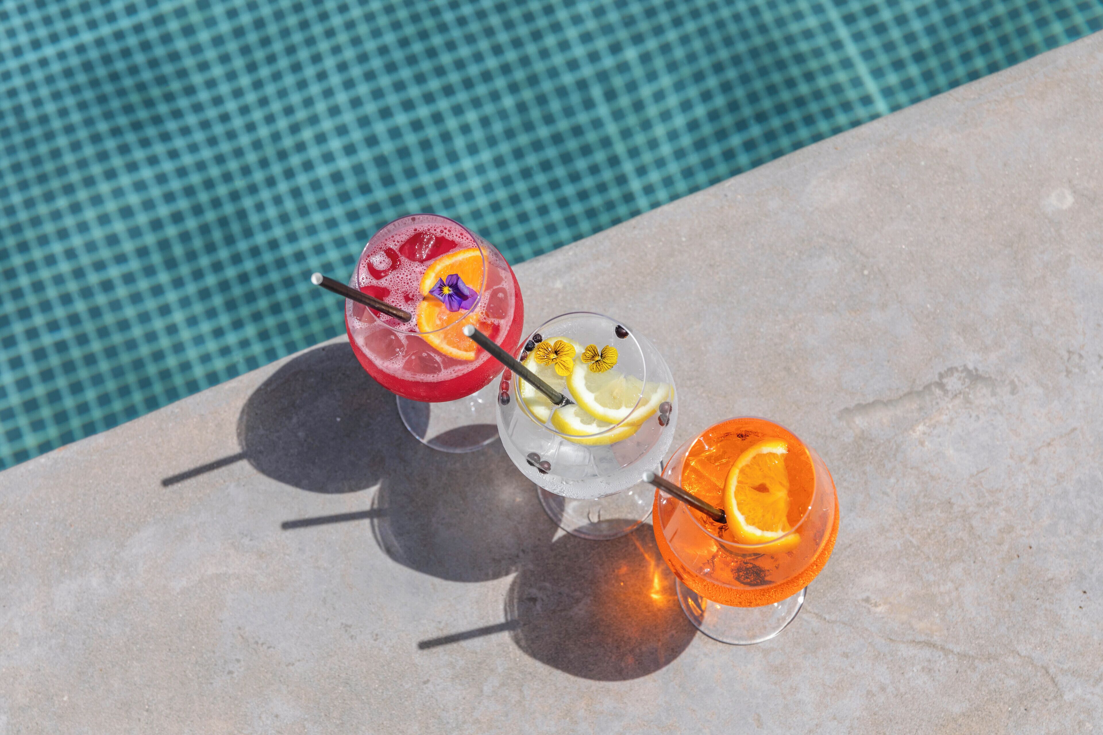 Three drinks on a stone surface near a pool.