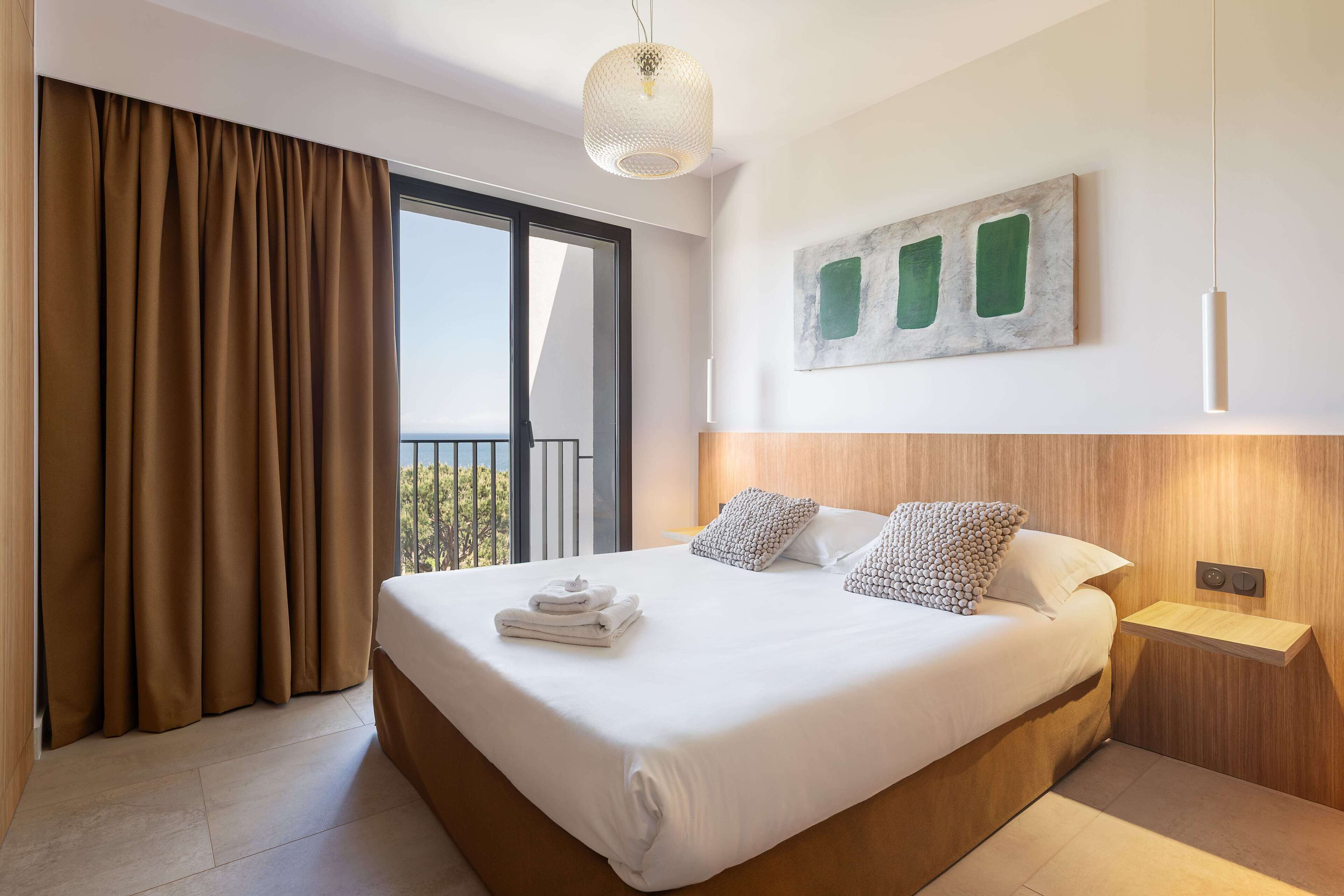 A hotel room with a large bed, a bedside table, a wall-mounted artwork, and a view through a sliding door.