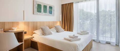 A modern hotel room with a large bed, a desk, and a view of the outdoors.