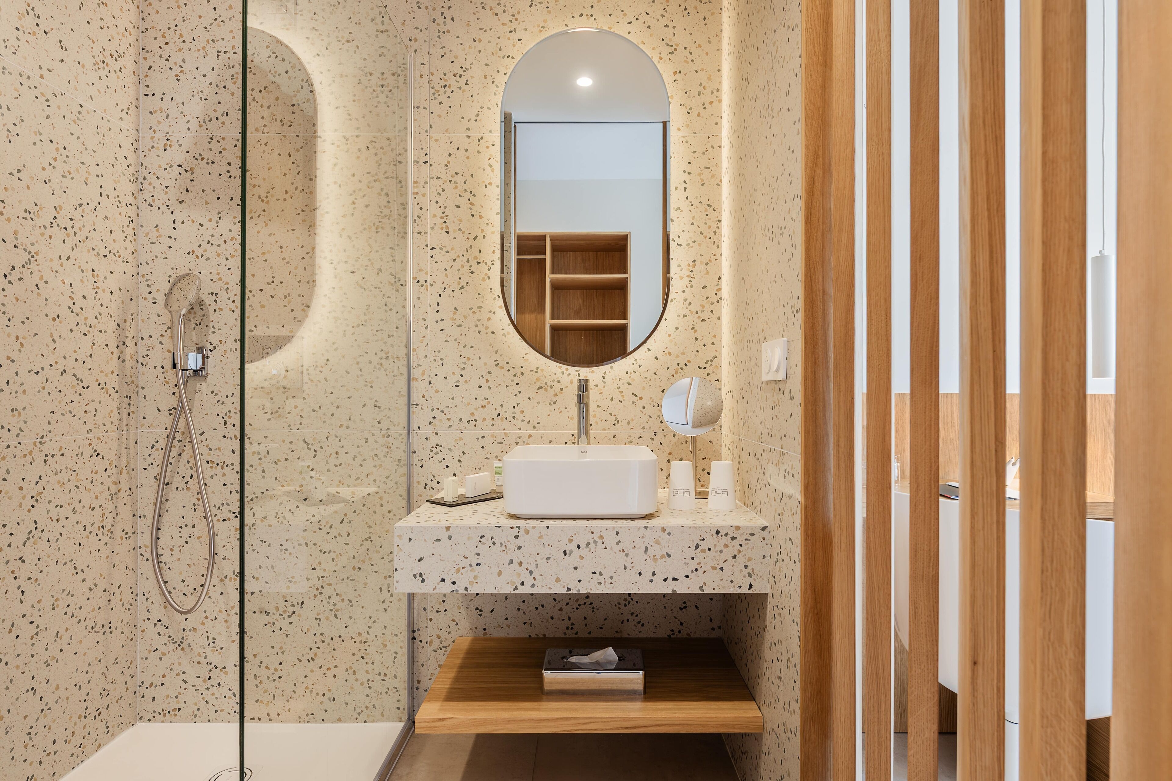 A modern bathroom with a freestanding shower, a round mirror, and a wooden vanity.