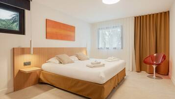 Ein modernes Hotelzimmer mit einem großen Bett, einem Nachttisch, einem roten Sessel und einem Fenster mit Vorhängen.