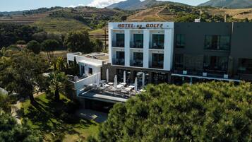 Un hotel moderno con terraza en la azotea, rodeado de vegetación exuberante y montañas al fondo.