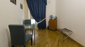 A room with a wooden floor, a blue curtain, a glass table, a blue chair, a wooden cabinet, and a metal drying rack.
