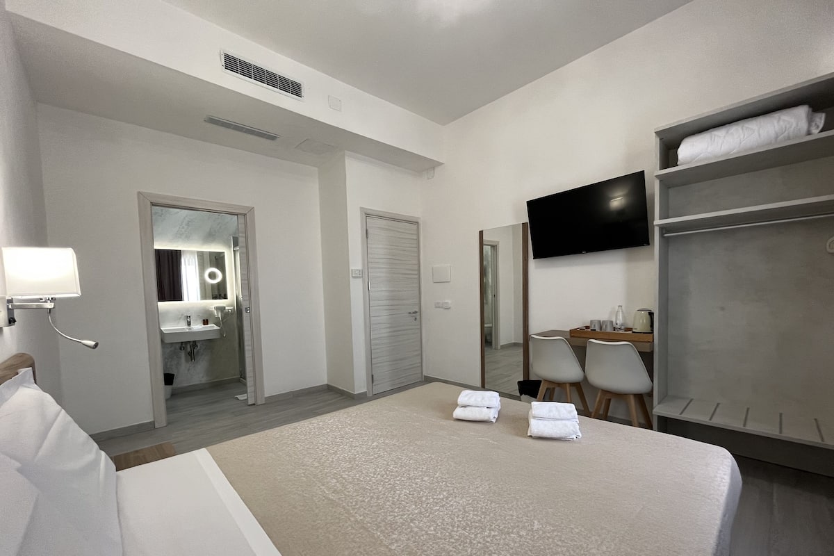 A hotel room with a bed, a desk, a TV, a mirror, and a wardrobe.