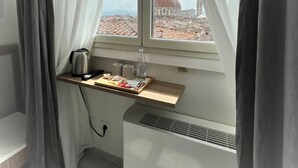 A room with a window overlooking a cityscape, featuring a radiator, a small table with a kettle, and a bottle of water. - Hotel Ester (Florence)