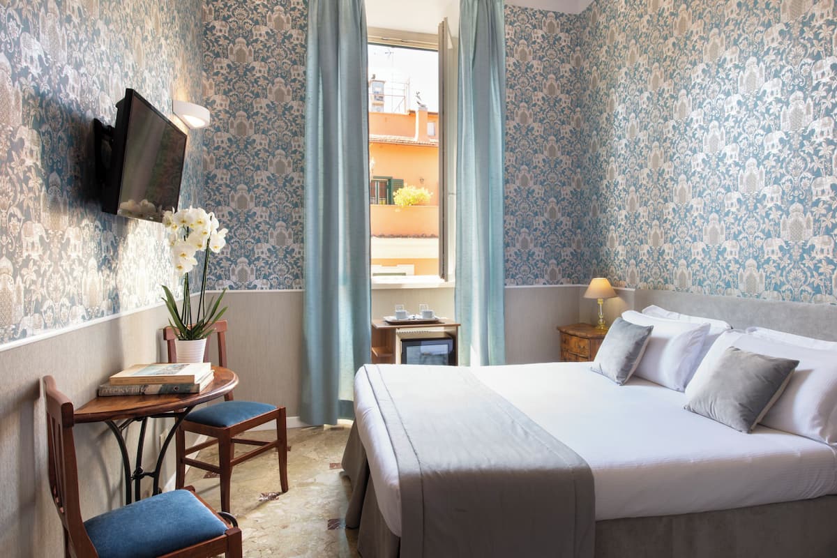 Ein Hotelzimmer mit Bett, Schreibtisch mit Stuhl, Wandfernseher und einem Balkon mit Vorhängen.