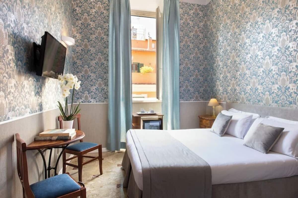 Ein Hotelzimmer mit Bett, Wandfernseher, einem kleinen Tisch mit Stühlen und einer Zimmerpflanze.