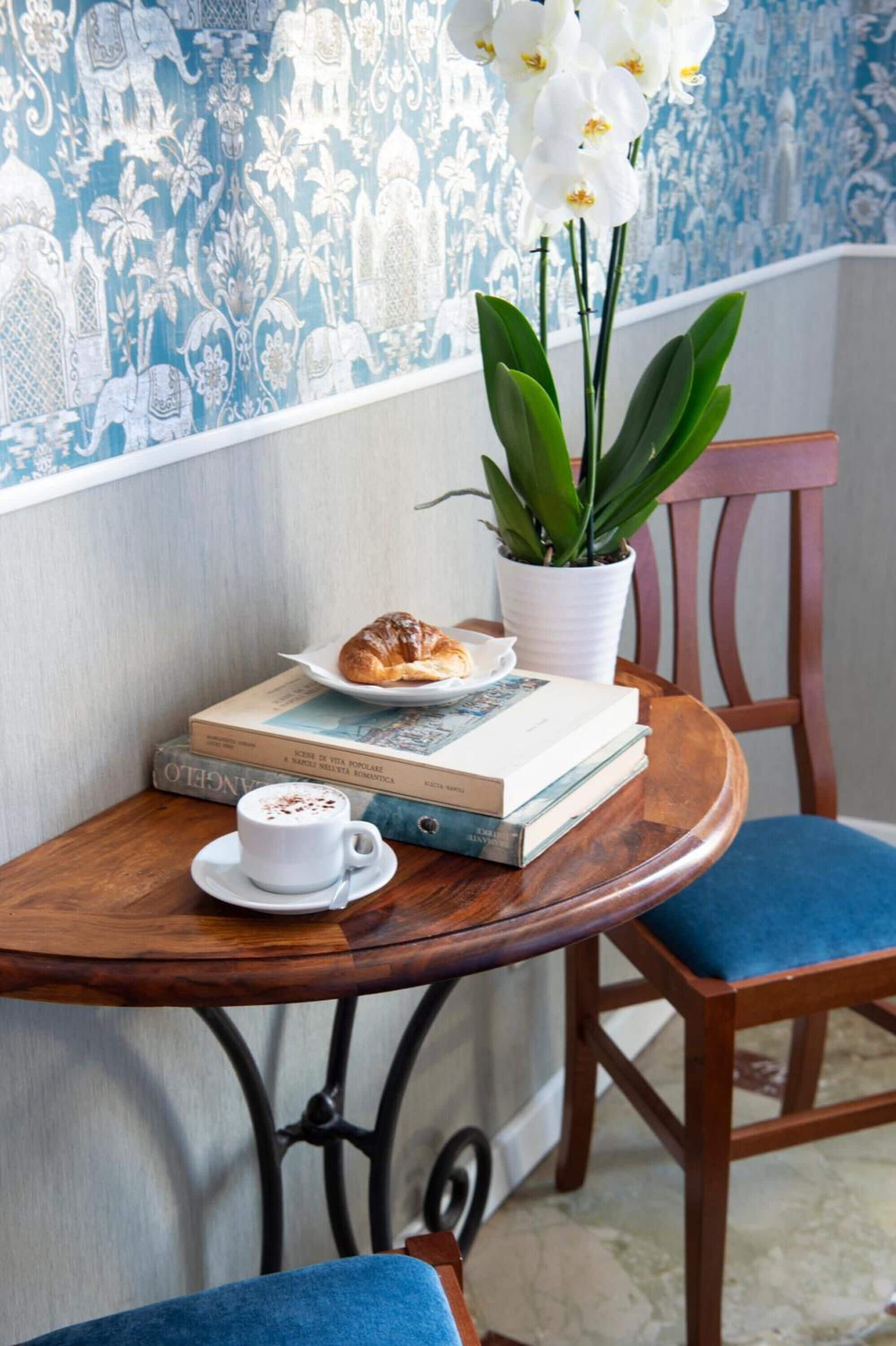 A wooden table with a white cup, a plate with a croissant, and a potted plant.