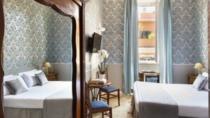 Ein Hotelzimmer mit zwei Betten, einem kleinen Tisch mit einer Pflanze und einem Fernseher an der Wand.