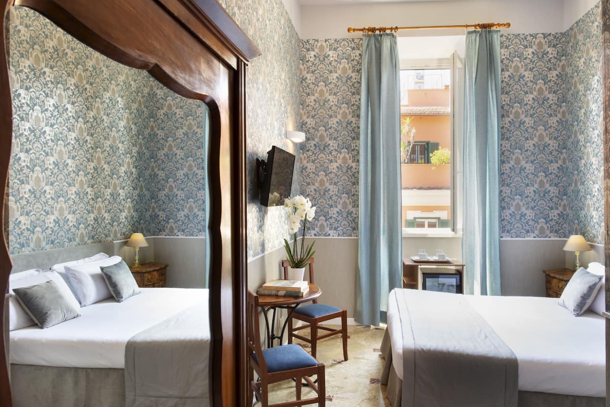 Ein Hotelzimmer mit zwei Betten, einem kleinen Tisch mit einer Pflanze und einem Fernseher an der Wand.
