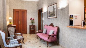 Ein Zimmer mit Holztür, einer Couch, einem Sessel, einem kleinen Tisch mit Blumenvase und einem an der Wand hängenden Bild.