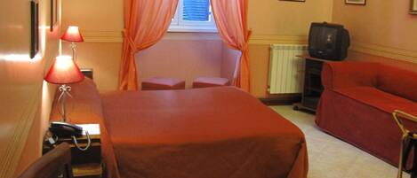 A hotel room with a bed, a desk with a lamp, a television, and a red sofa.