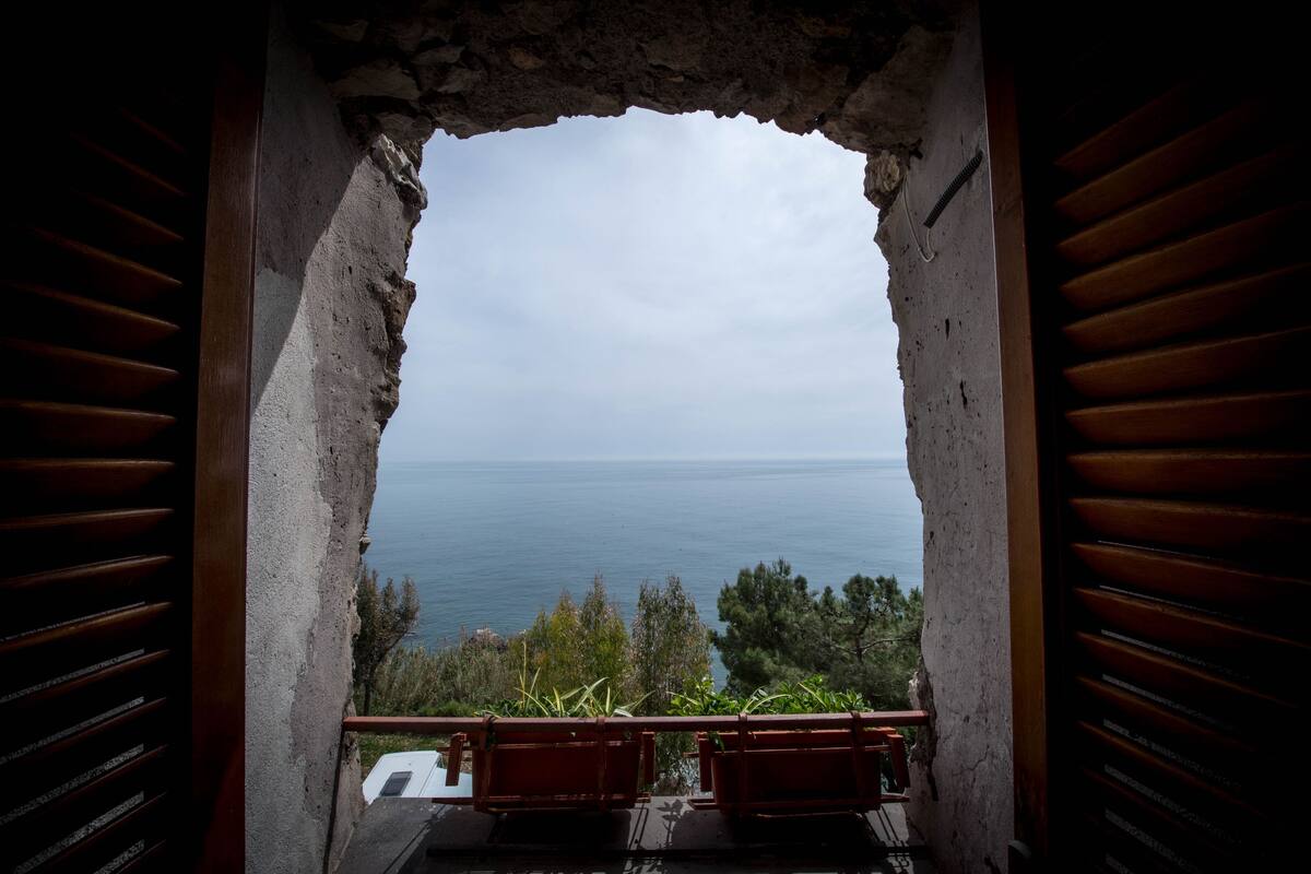 A balcony with a view of the sea, a rustic stone wall, and wooden shutters.