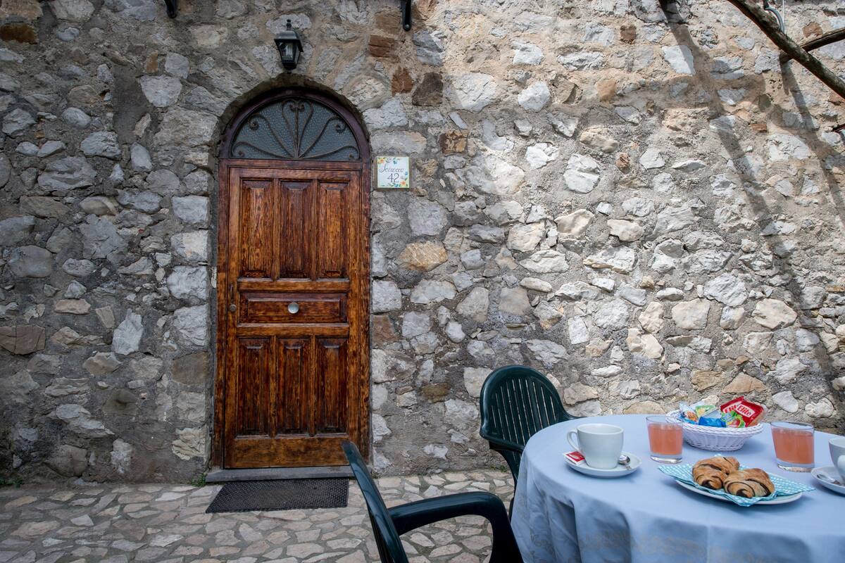 A stone wall with a wooden door, a table with a basket of pastries, and two cups of tea.