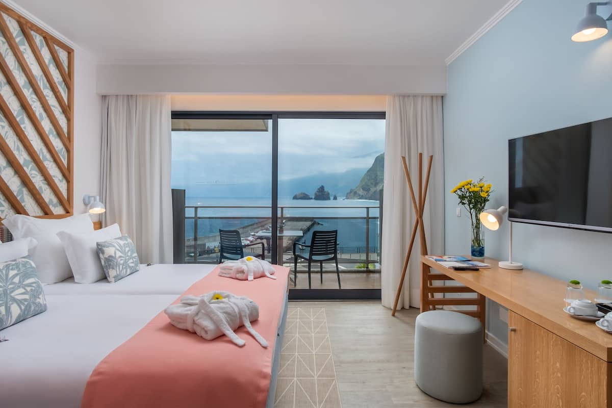 Habitación de hotel con cama, escritorio, televisión y balcón con vista al mar.