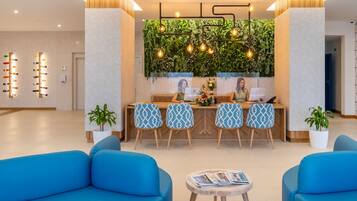 Un espace d’accueil moderne avec un comptoir de réception en bois, des chaises à motifs et un mur végétal agrémenté de luminaires suspendus.