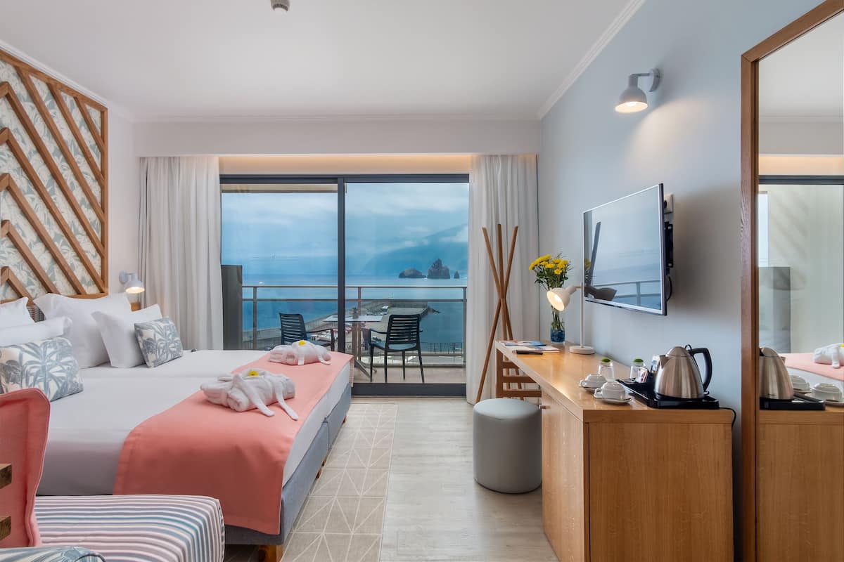 Habitación de hotel con cama, escritorio, silla, televisor y balcón con vista al mar.