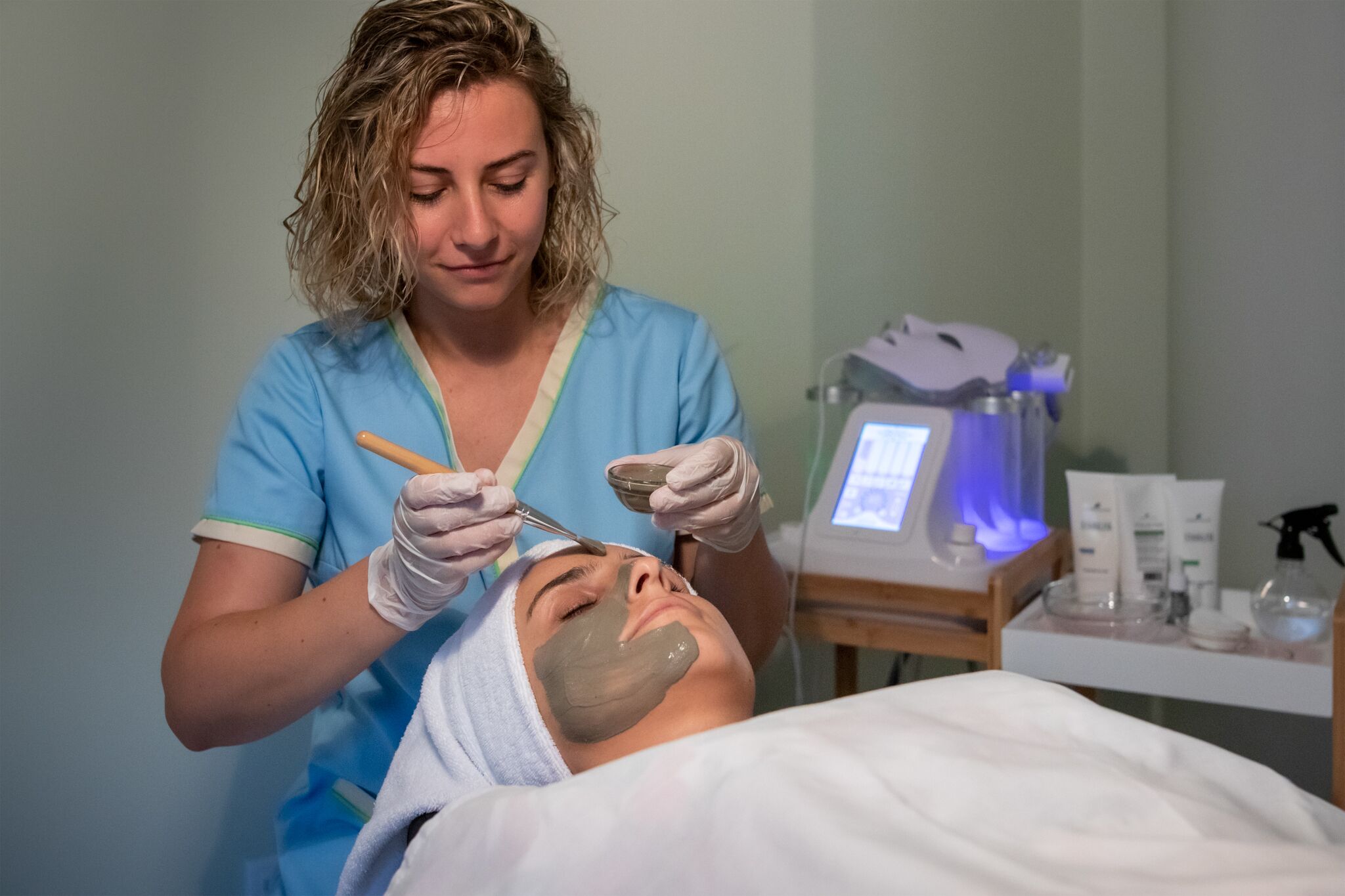 A person receiving a facial treatment in a clinical setting with medical equipment and supplies visible.
