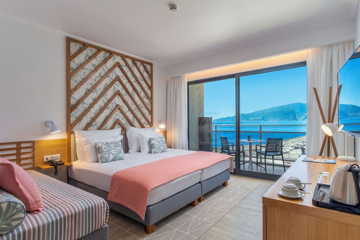 Habitación de hotel con cama, escritorio, silla, una mesita y vista al mar.