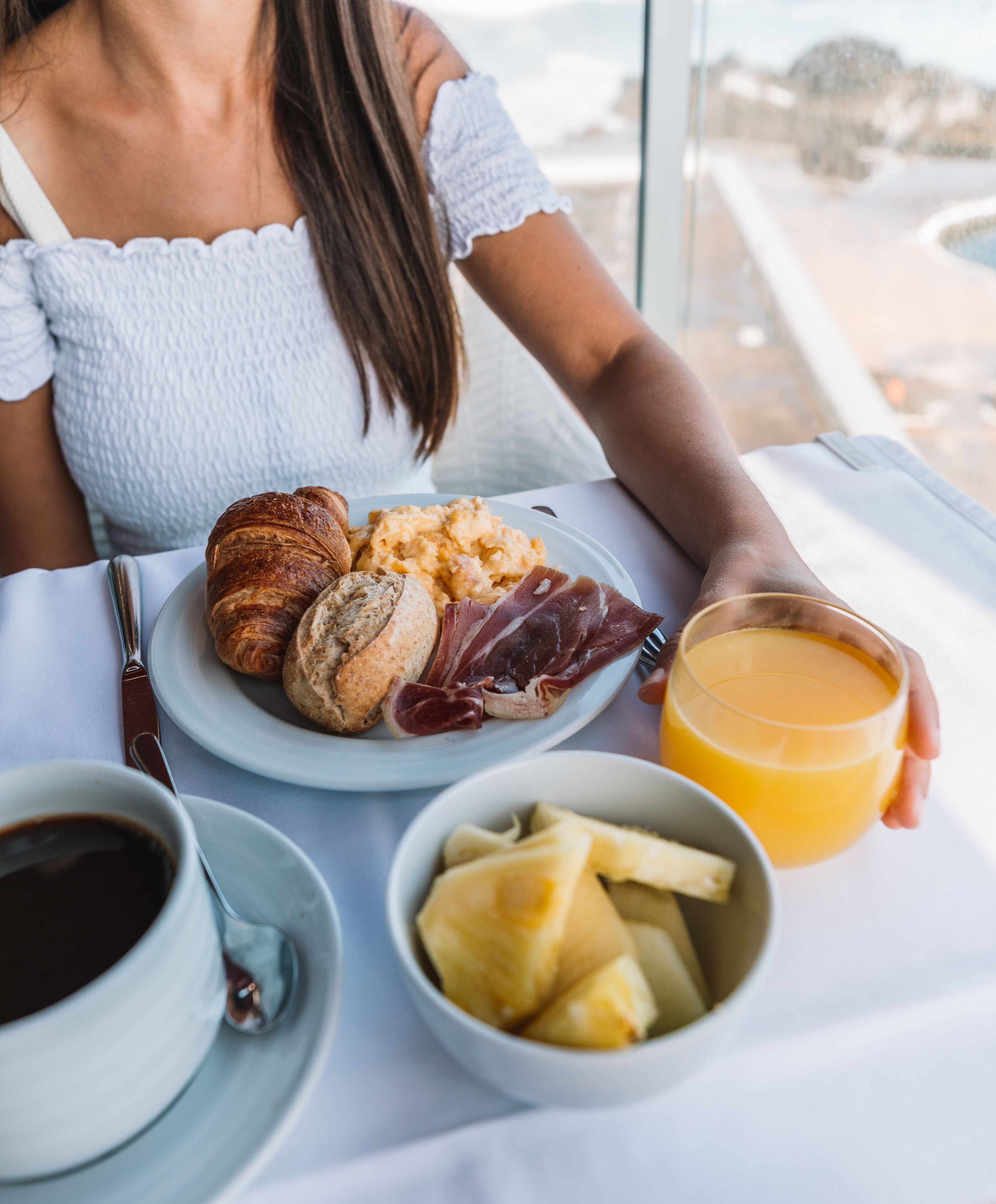 Un desayuno con croissants, jamón, huevos revueltos y jugo de naranja sobre una mesa.